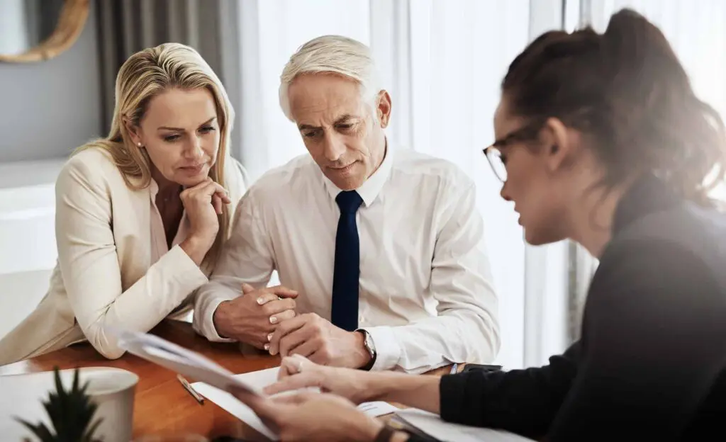 Adult couple holding hands and looking at documents being presented to them by a business women