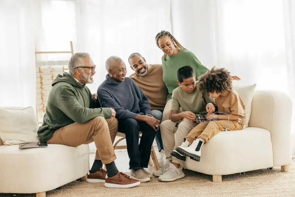 Three generations of a family sitting in the living room focused on a toy held by the youngest family member.
