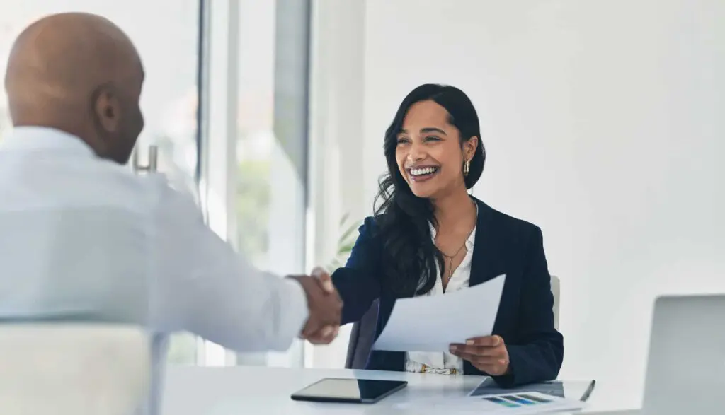 Women smiling and holding a document while shaking hands with a man sitting across the table