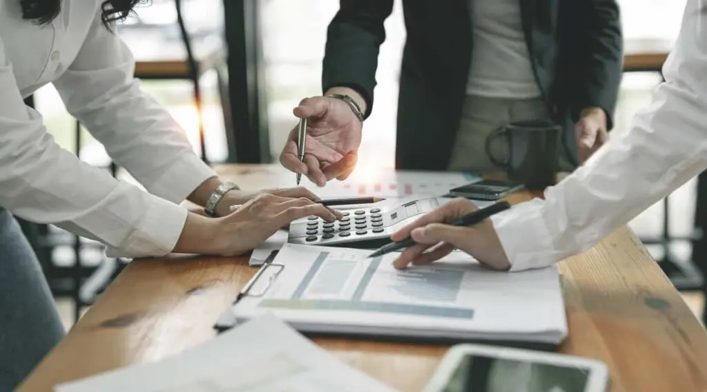 Close up of three people pointing to a document and a calculator in an office