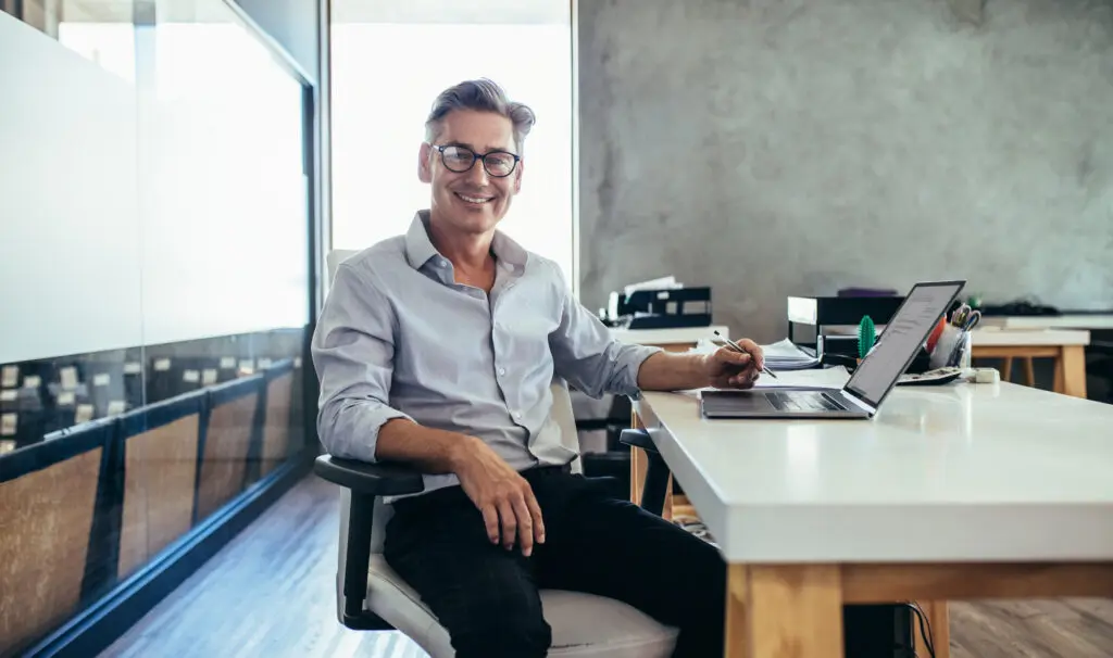 Business man sitting in an office with his laptop open looking directly at the camera