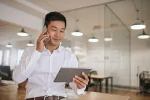 Asian business man on the phone while looking at a tablet in a modern office