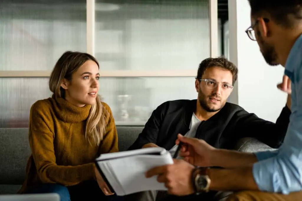 A woman with a yellow sweater and a man in a black jacket talking to a banker with a notebook