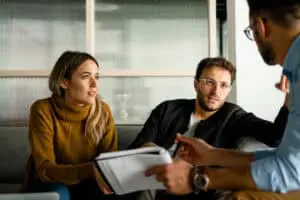 A woman with a yellow sweater and a man in a black jacket talking to a banker with a notebook