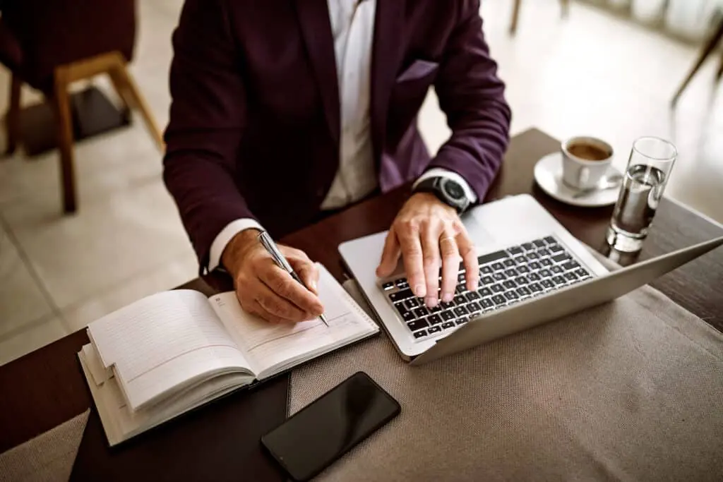 Senior businessman using laptop in lobby of hotel while drinking coffee