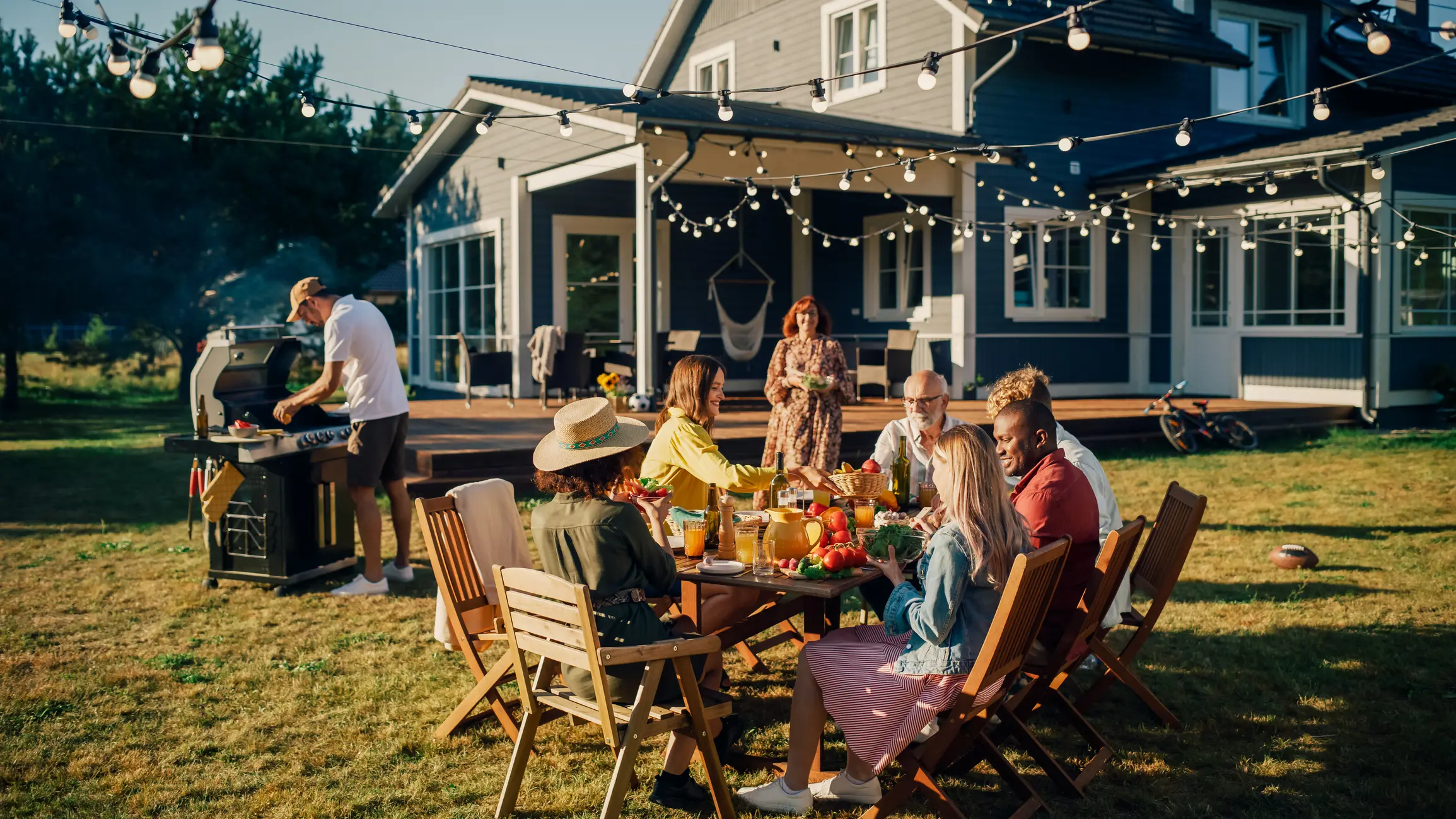 Group of Multiethnic Diverse People Having Fun, Communicating with Each Other and Eating at Outdoors Dinner. Family and Friends Gathered Outside Their Home on Warm Summer Day.