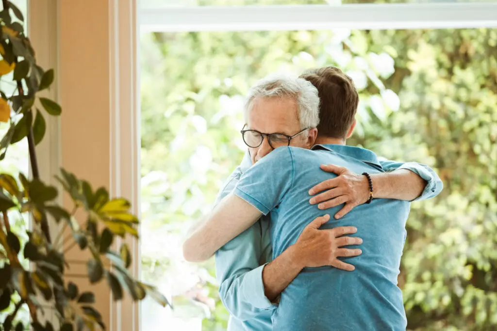 Senior man hugging son against window at home