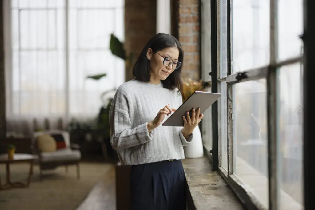 Chinese woman surfing the Internet on digital tablet by the window at home.