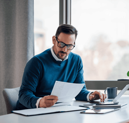 Business man in a blue sweater looking at documents while on the computer