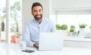man looking at camera at home with computer in front of him