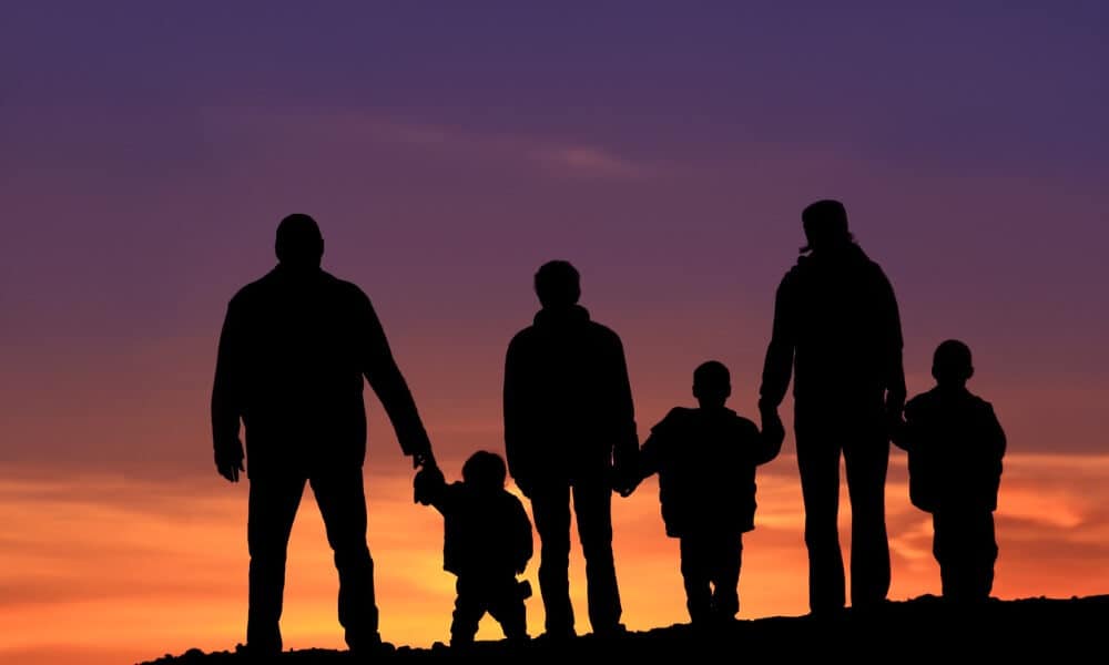 Family standing on hill holding hands while sun is setting