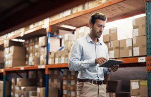 business man in supply chain warehouse looking at tablet surrounded by packages