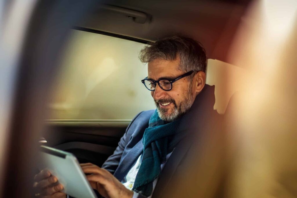 Man looking at a tablet and smiling while in the backseat of a car