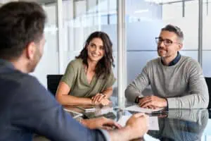 Smiling mature couple meeting with bank manager for investment. Beautiful mid adult woman with husband listening to businessman during meeting in conference room in modern office. Happy middle aged couple meeting loan advisor to buy a new home.