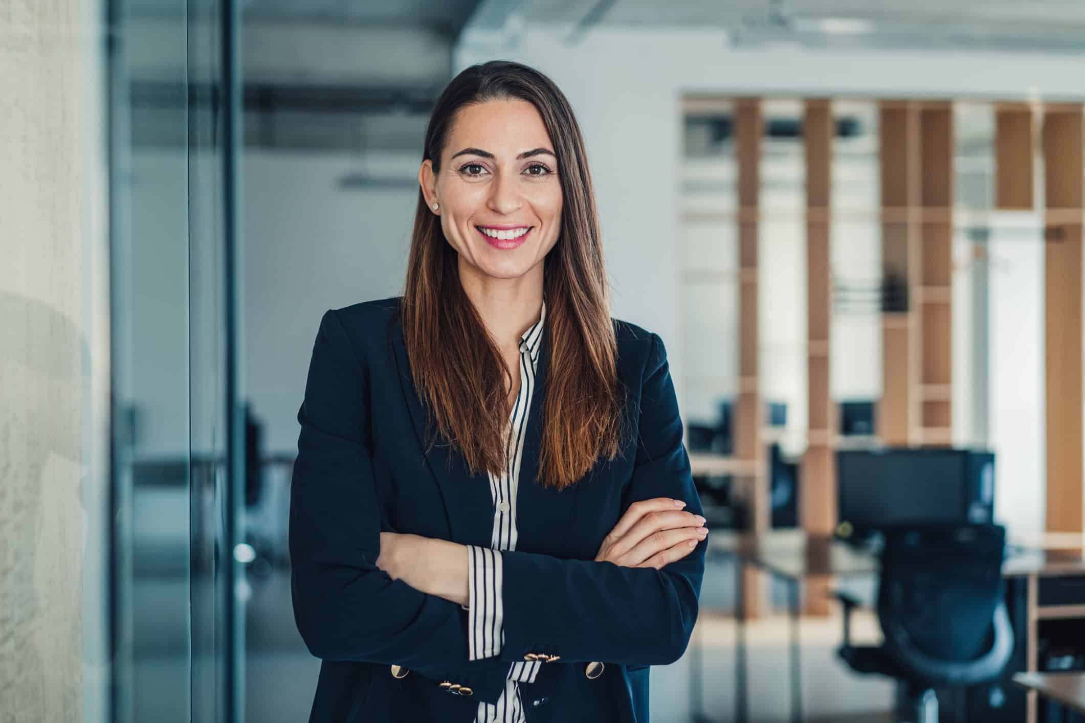 Shot of smiling businesswoman standing with crossed arms in her office and looking at camera.