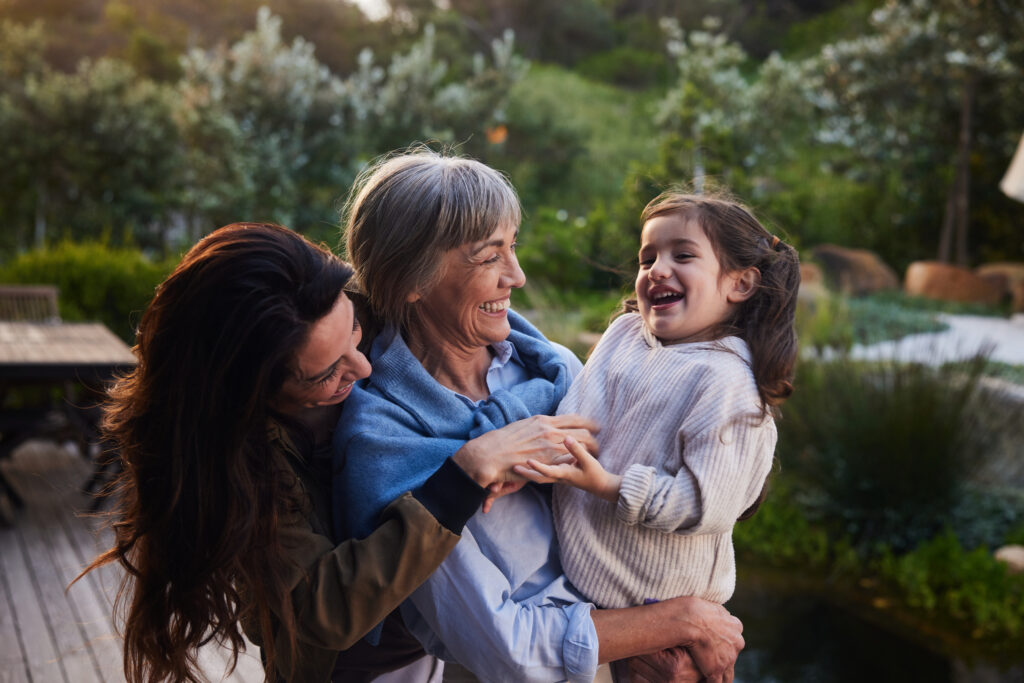 Little girl laughing while standing outdoors with her grandmother and mom