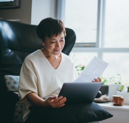 Asian woman looking at a paper and laptop at home