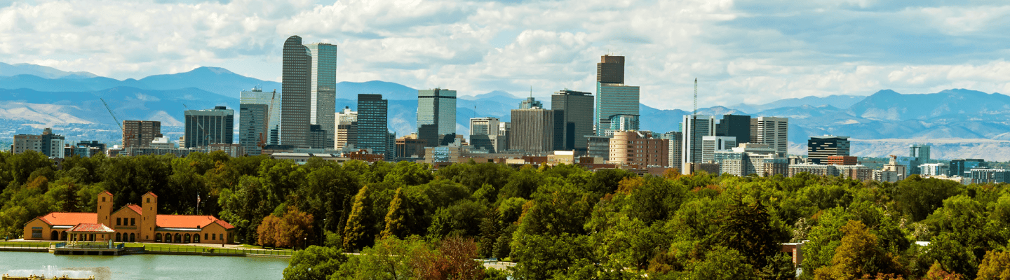 Denver skyline with trees in the foreground and mountains in the background