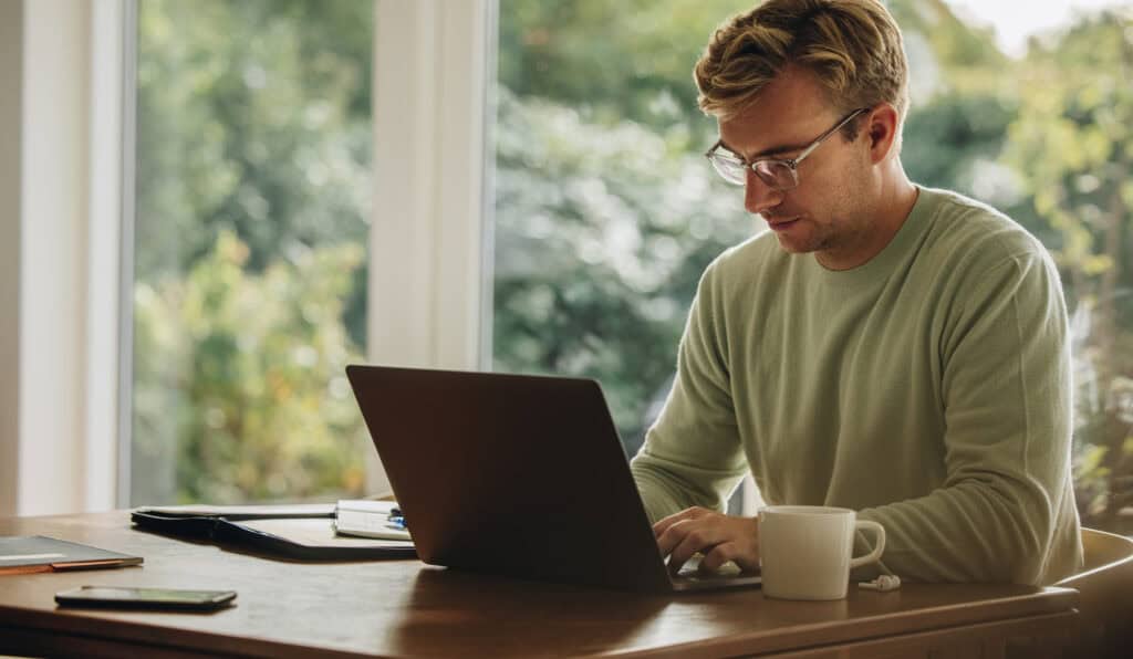 Young man working on laptop. Man sitting at table and using laptop while at home.